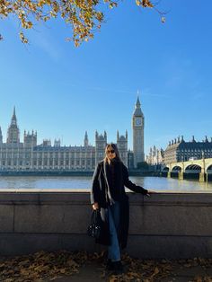 a woman standing on the edge of a bridge next to a body of water with big ben in the background