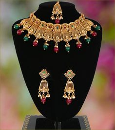 "This Gorgeous dream necklace set with an intricate design in 22KT gold plating. This high quality choker necklace deco intermittently studded around with ruby and emerald round synthetic stones and complete with pair of matching earrings and tikka. 1 x Necklace approx. 5 inches Collar-Wide . Back adjustable rope is attached. 1 x Pair of Earrings 2.75\" Length from top to bottom. *Adjustable & Appropriate for All Neck Sizes. Perfect for a bride in wedding or party wear jewelry set." Traditional Ruby Jewelry Sets With Intricate Design, Gold Ruby Necklace With Intricate Design, Elegant Jeweled Ceremonial Temple Necklace, Elegant Gold Emerald Meenakari Necklace, Elegant Gold Emerald Necklace With Meenakari, Ruby Temple Jewelry With Intricate Design, Gold Emerald Necklace With Intricate Temple Jewelry Design, Festive Ruby Jewelry Set With Intricate Design, Ornate Metal Jewelry For Wedding