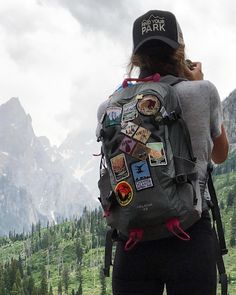 a woman wearing a backpack with many stickers on it and mountains in the background