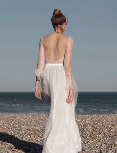 the back of a woman in a white wedding dress standing on rocks near the ocean