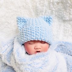 a newborn baby wearing a blue knitted hat and sleeping on a white fluffy blanket