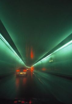 a car driving through a tunnel in the rain at night time with green lights on it's sides