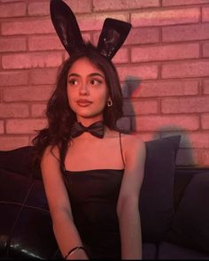 a woman wearing bunny ears sitting on top of a black couch next to a brick wall