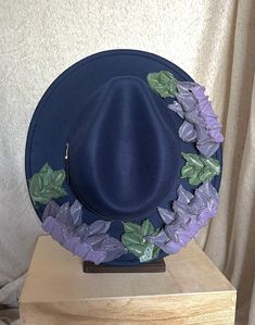 This one of a kind, hand painted, textured floral fedora is the perfect walking art piece. Each hat is uniquely crafted and perfect for any occasion.  This navy blue fedora is crafted with soft glittered purples, lavender, and green accents. These island treasures are shipped straight to you from the Hawaiian island of Oahu. (Hats are water resistant. Keep out of heavy rain. Spot clean only) Blue Brimmed Felt Hat For Kentucky Derby, Blue Adjustable Fedora For Kentucky Derby, Blue Hat For Kentucky Derby Festival, Blue Hat For Kentucky Derby, Whimsical Flat Brim Fedora For Kentucky Derby, Artistic Fedora With Short Brim For Spring, Artistic Brimmed Fedora For Spring, Adjustable Blue Fedora For Spring, Artistic Wide Brim Fedora For Spring