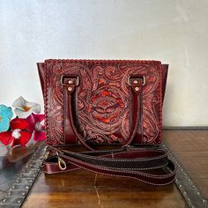 Get your hand on this one of a kind, ravishing and elegant leather bag that is a true head turner. The spectacular hand tooled leather work is a mural of floral beauty. A soft suede interior. We're confident you will fall in love MADE IN MEXICO By: Mexican Artisans For: Women Color: red brown Dimensions: 13 x 9.5 x 4 Details: 100% Authentic Leather Style: Top-Handle | Tote | Shoulder Bag Embossed Design Top Handles: 7" Drop Adjustable & Removable Strap: 24" Drop Interior: Soft Suede Zipper Closu Formal Leather Embossed Shoulder Bag, Formal Embossed Leather Shoulder Bag, Hand Tooled Top Handle Satchel, Burgundy Leather Handheld Satchel, Red Hand Tooled Rectangular Bag, Hand Tooled Red Rectangular Bag, Red Hand-tooled Rectangular Bag, Hand Tooled Leather Top Handle Satchel, Red Hand Tooled Bag For Daily Use