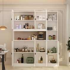 a white shelf filled with lots of different types of items next to a chair and table