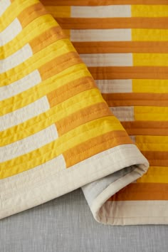 an orange and white striped quilt on top of a gray bed sheet with two pillows