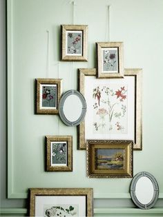 several framed pictures hang on the wall above a table with a clock and other items