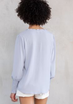 Designed in ultra-soft and silky crepe, this effortless bohemian peasant top is an instant classic. Featuring a delicate self-covered button front detail, voluminous long sleeves with a smocked elastic wrist cuff, and smocking along the shoulder. Try this versatile style tucked into trousers or untucked over jeans. Silky crepe Relaxed fit Long voluminous sleeve Smocked elastic wrist cuff Split v-neckline with ties Ruffled neckline Self-covered button front Smocked shoulder details Bohemian resor Fall Balloon Sleeve Smocked Top With Smocked Cuffs, Flowy Smock Blouse, Flowy Puff Sleeve Blouse With Smocked Bodice, Flowy Blouse With Smocked Bodice And Puff Sleeves, Spring Balloon Sleeve Blouse With Smocked Cuffs, Billowy Lantern Sleeve Blouse With Elastic Sleeves, Feminine Smocked Top For Fall, Flowy Puff Sleeve Tops With Elastic Sleeves, Flowy Blouse With Smocked Cuffs For Spring