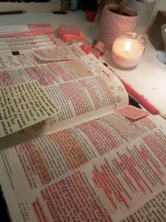 an open book sitting on top of a table next to a candle and some papers