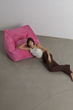 a woman laying on the floor next to a pink bean bag chair in an empty room