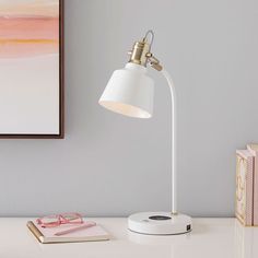 a white desk lamp sitting on top of a table next to a pink and yellow painting