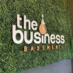 the business basement sign is mounted on a wall with green plants in front of it