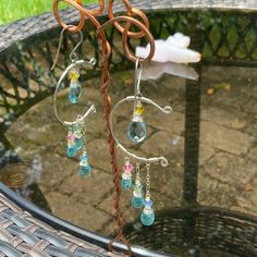 a pair of earrings is sitting on a glass table with some wire and beads hanging from it