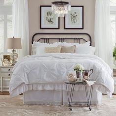 a white bed in a bedroom with two pictures on the wall above it and an end table