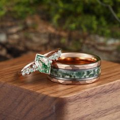 two wedding rings sitting on top of a wooden table next to another ring with green and white stones