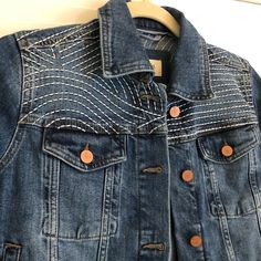 a denim jacket with buttons on the front and back, hanging from a hanger