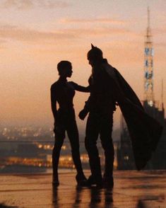 two people standing next to each other in front of a cityscape at sunset