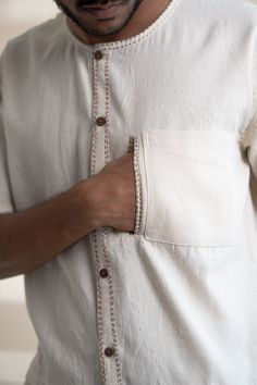 This Dawning Layered Shirt comes in a calm and soothing color. This layered shirt with an interesting play of panelling of two fabrics, Kala Cotton and self-checked, is undyed and unbleached. Replete with a classic round neck, this half-sleeve shirt comes with two functional pockets. Stitches of Kantha, a form of Indian hand embroidery, line the placket, neckline and pockets. *This item is a final sale and not eligible for returns or exchanges. *This item can take up to 14 business days to ship Men Embroidery Shirts, Shirt Pocket Embroidery, Mens Shirt Details, Indian Hand Embroidery, Linen Kurti, Embroidery Shirt Men, Menswear Details, Gents Kurta, Linen Embroidery