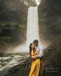 a man and woman standing in front of a waterfall