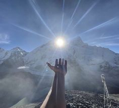 a hand reaching up towards the sun with mountains in the background