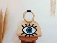 a handbag with an eye painted on the front and side, sitting on top of a wooden stand