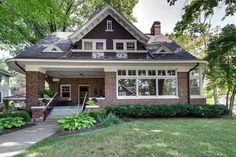 a small brick house with white trim and windows in the front yard, surrounded by lush green trees