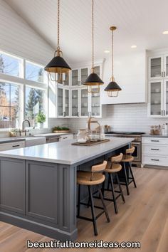 a large kitchen with white cabinets and wooden flooring, two pendant lights hanging over the island