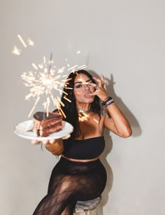 a woman sitting on a stool holding a piece of cake with sparklers in her hand