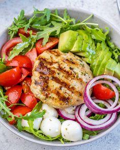 a white bowl filled with salad and meat topped with tomatoes, onions, cucumbers, lettuce