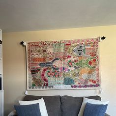 a living room with a gray couch and colorful tapestry hanging on the wall above it