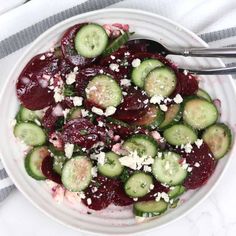 a white plate topped with beets and cucumbers covered in feta cheese