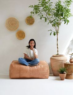 a woman sitting on top of a bean bag chair next to potted plants and wall hangings