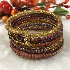 Created with a selection of brown, gold, and purple-ish glass beads on a gold-toned wire, finished with a cute leaf charm. One-of-a-kind! One continuous stainless steel wire makes 10 loops around the wrist, giving the appearance of 10 stacked bracelets. Memory wire holds its shape over time and is nearly impossible to break.  One size fits most. Makes a great gift! Includes white gift box. Memory Wire Wrap Bracelets Color Combos, Gold Bohemian Wrap Bracelet With Spacer Beads, Gold Multi-strand Stackable Beaded Bracelets, Adjustable Gold Beaded Copper Bracelets, Gold Wire Wrapped Beaded Bracelets, Gold Wire Wrapped Beaded Bracelets With Round Beads, Bohemian Gold Beaded Copper Bracelets, Bohemian Gold Beaded Bracelets Wire Wrapped, Bohemian Gold Beaded Wire Wrapped Bracelets