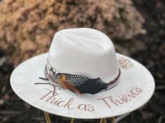 "The Lainey Wilson Concert Wide Brimmed Cowgirl Hat - Thick as Thieves design is perfect for attending that upcoming Lainey concert... Or just displaying your fan crush!   Colors: Cream Sand (Light Tan) Cognac (Dark Tan) Each hat displays the \"Thick as Thieves\" lettering and a floral arrangement burned-by-hand around the hat brim, as well as, a Lainey Wilson concert ticket stub. Flowers are just my creative arrangements, but feel free to let me know if you have a specific flower that you would Lainey Wilson Hats, Lainey Wilson Concert, Hat Displays, Thick As Thieves, Custom Cowboy Hats, Hat Bar, Concert Attire, Lainey Wilson, Concert Ticket