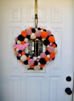 a decorated wreath on the front door of a house with pink and orange pom - poms