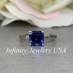 an image of a ring with a blue stone in it on a table next to flowers