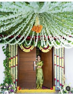 a woman in a green sari standing at the entrance to a building with flowers on it