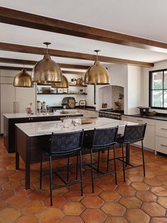 a large kitchen with an island in the middle and gold pendant lights hanging from the ceiling