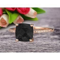 a black diamond ring sitting on top of a wooden table next to flowers and pink tulips