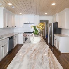 a kitchen with white cabinets and marble counter tops, along with an island in the middle