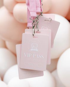 two tags attached to a pink ribbon with white balloons in the back ground behind them