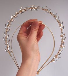 a hand holding a gold headband with silver leaves on it's sides,