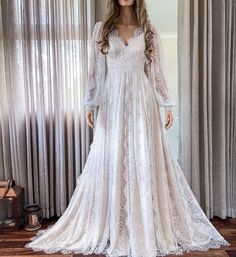 a white wedding dress with long sleeves on display in front of a curtained window