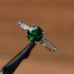 a close up of a ring with a green stone in the middle and diamonds around it