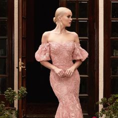 a woman standing in front of a door wearing a pink dress with off the shoulder sleeves