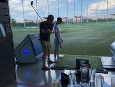 two people standing in front of a tv set with golf equipment on the table next to them