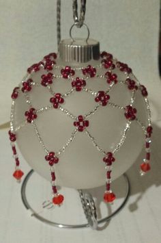 a white ornament with red beads and silver chain hanging from it's holder