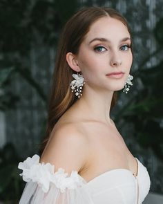 a woman in a white dress with flowers on her shoulder and earring, looking off to the side