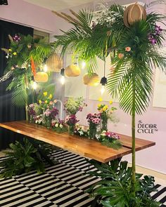 a table topped with lots of potted plants next to a wall filled with lights